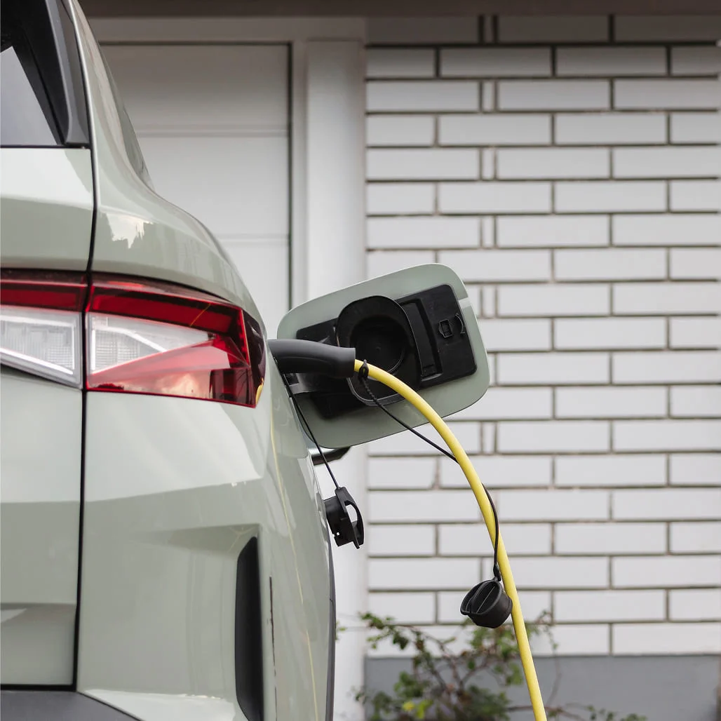 A light green electric vehicle plugged into a yellow charging cable.