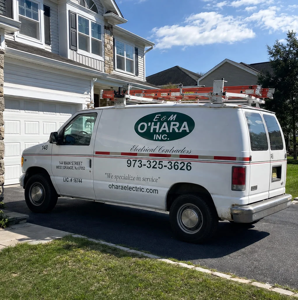 A white E & M O’Hara Inc. electrical contractor van with a ladder rack parked in a residential driveway.
